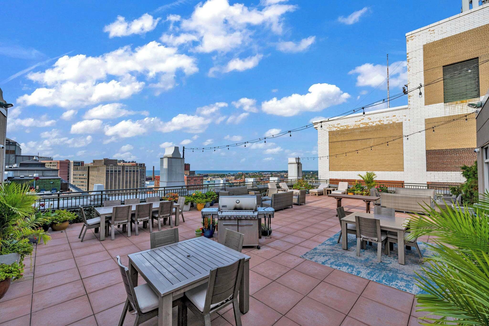 A rooftop patio with outdoor furniture, a grill, and potted plants.