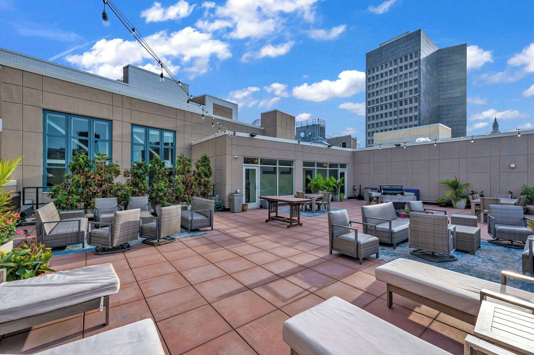 Una terraza en la azotea con mobiliario exterior, plantas en macetas y vistas a un paisaje urbano.