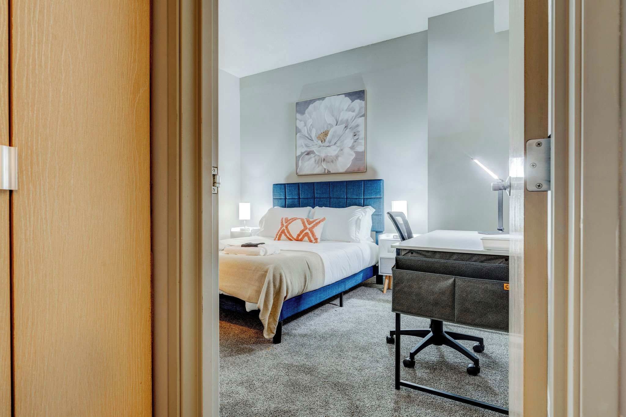 A modern hotel room with a bed, bedside table, and a desk with a chair.