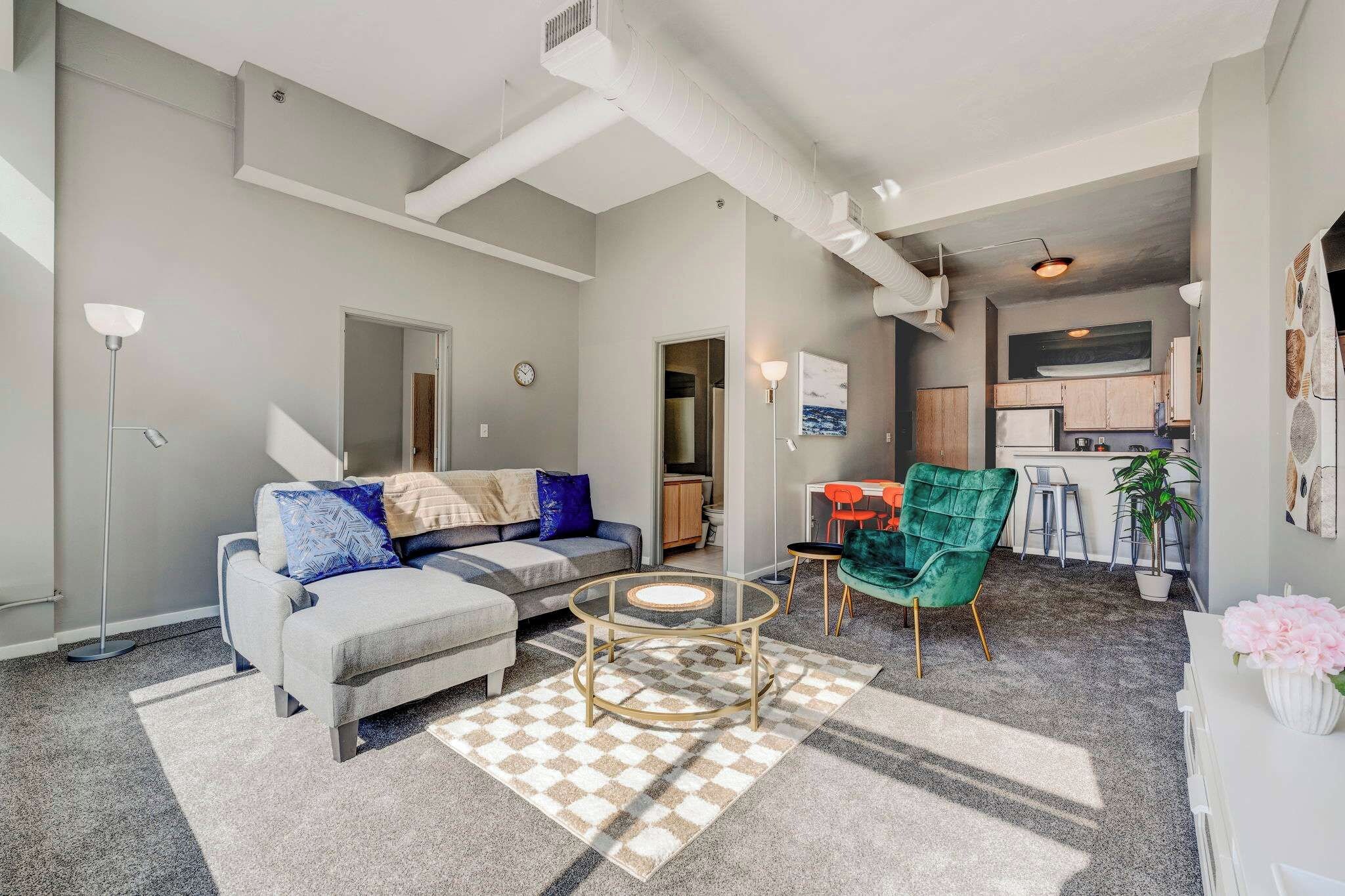 A modern living room with a grey sofa, a glass coffee table, and a checkered rug.