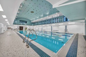 An indoor swimming pool with a tiled floor, a pool ladder, and a ceiling with circular lights. - HUGE Loft in Heart of Downtown • Pool/Sauna • Gym (Cleveland)
