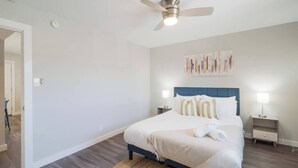 A bedroom with a bed, a ceiling fan, bedside lamps, and a wall-mounted artwork.