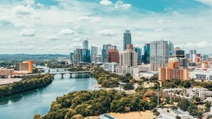A city skyline with modern high-rise buildings, a river, and a bridge.