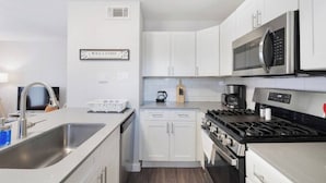 A modern kitchen with white cabinets, stainless steel appliances, and a welcome sign.