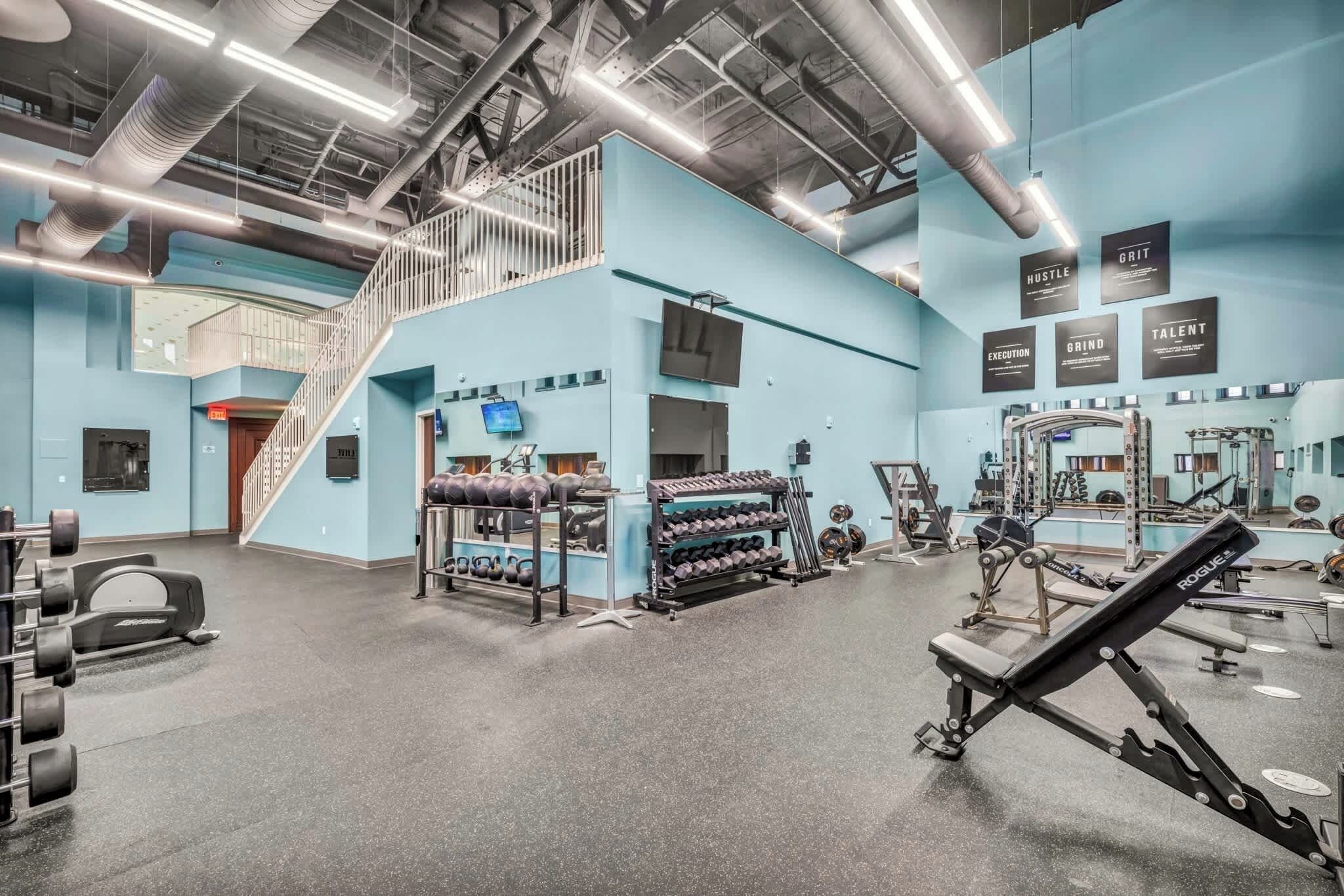 Une salle de sport équipée de matériel de musculation, avec un escalier et des œuvres d’art murales inspirantes.