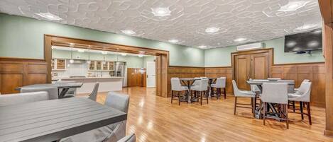 A spacious dining area with wooden flooring, a modern ceiling design, and a kitchen visible in the background.