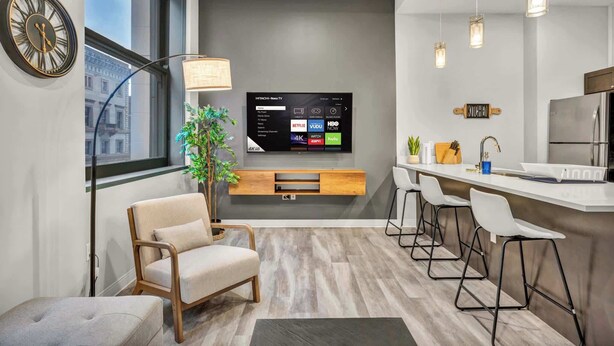 A modern living room with a TV, seating, and a kitchen area. - Central Flat w/ Pool & Sauna • Gym•Heart of DT (Cleveland)