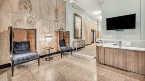 A hotel lobby with a reception desk, two seating areas with chairs, a large mirror, and a television mounted on the wall. - Central Flat w/ Pool & Sauna • Gym•Heart of DT (Cleveland)