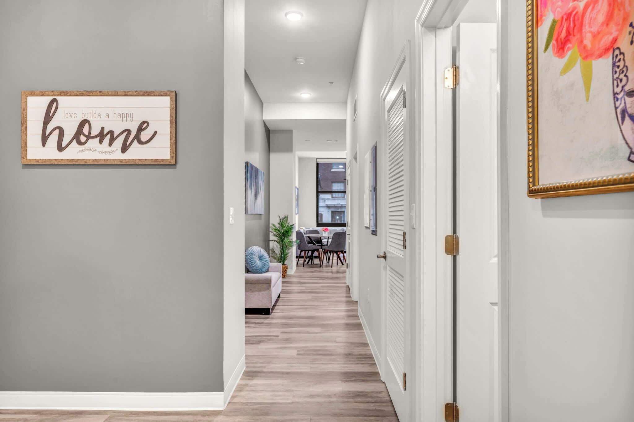 A hallway with a framed sign saying "love builds a happy home," a dining area with a table and chairs, and a door with a decorative painting.