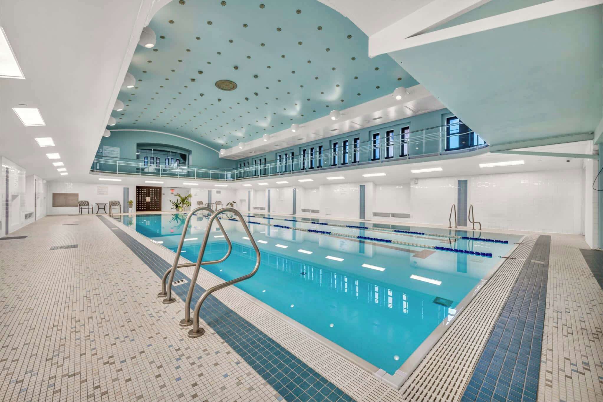 An indoor swimming pool with a tiled floor, a pool ladder, and a ceiling with circular lights.