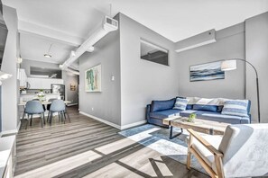 A modern living room with a blue sofa, a wooden coffee table, and a dining area with a white table and chairs.