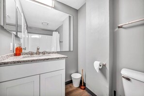 A modern bathroom with a granite countertop, a white toilet, a white bucket, and a plunger.