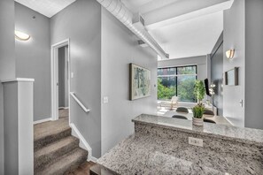 A modern interior with a staircase, a kitchen area with granite countertops, and a large window offering a view of greenery outside. - Huge Loft in Heart of Downtown • Pool & Spa • Gym (Cleveland)