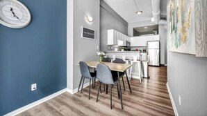 A modern kitchen with white cabinets, a dining area with a wooden table and grey chairs, and a wall-mounted clock. - Huge Loft in Heart of Downtown • Pool & Spa • Gym (Cleveland)