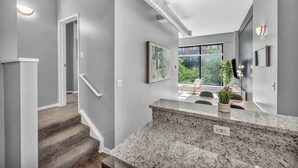 A modern interior with a staircase, a kitchen area with granite countertops, and a large window offering a view of greenery outside. - Huge Loft in Heart of Downtown • Pool & Spa • Gym (Cleveland)