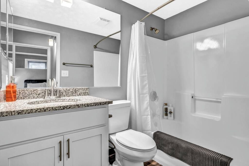 A modern bathroom with a white toilet, granite countertop, and a shower curtain.