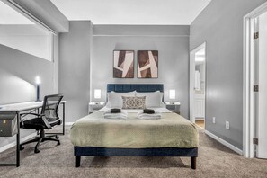 A modern bedroom with a large bed, a desk, and a chair. There are two bedside tables with lamps.