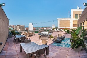 A rooftop patio with outdoor furniture, a grill, and a view of the cityscape.