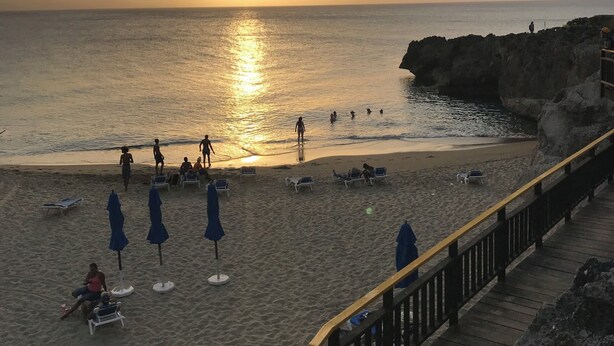 A beach with a wooden walkway, sunlit sand, and a calm sea at sunset.