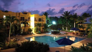 A hotel with a swimming pool, palm trees, and a sunset sky.
