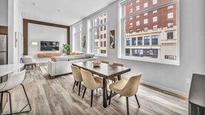 A modern living room with a dining area, large windows, and a city view. - Central Flat with Pool, Sauna, Rooftop Deck, Gym (Cleveland)