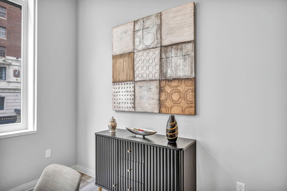 A room with a modern black console table, a decorative wall piece, and a window with a view of a building.