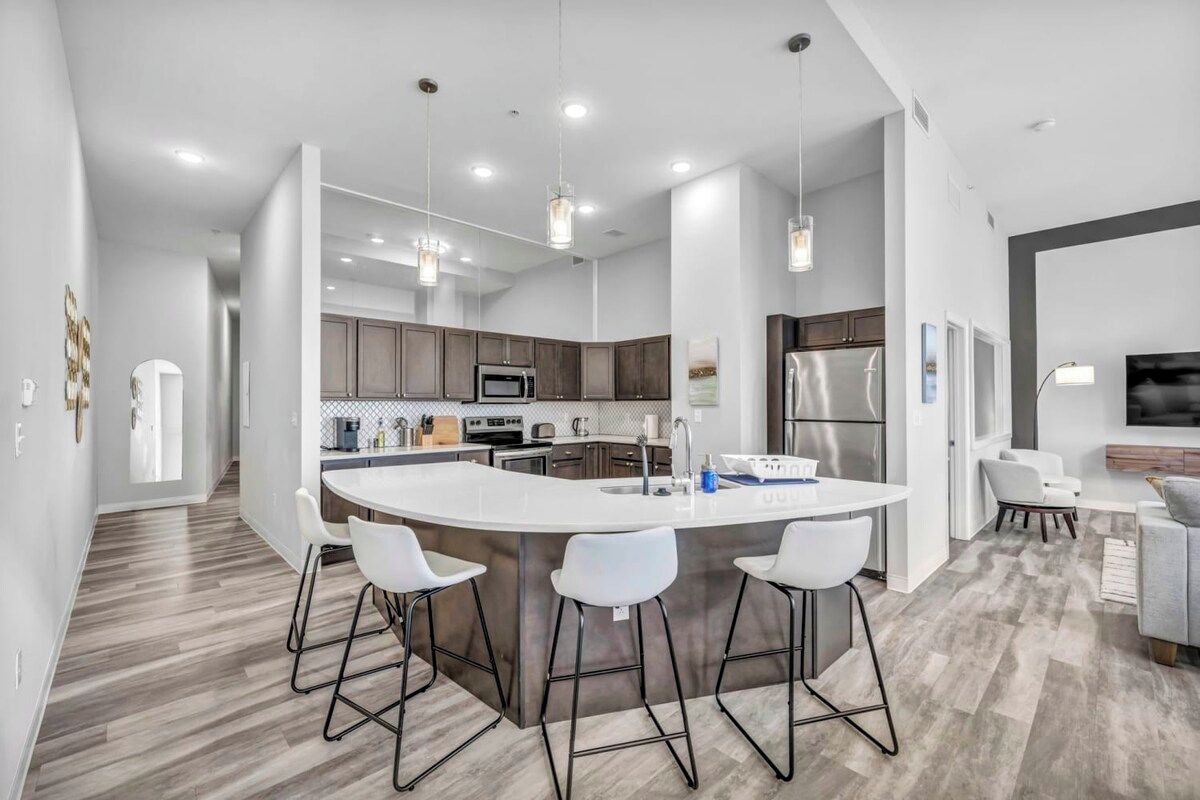 A modern kitchen with a large island, bar stools, and stainless steel appliances.