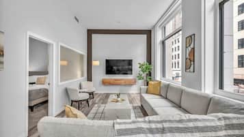 A modern living room with a large sofa, a coffee table, and a TV mounted on the wall.