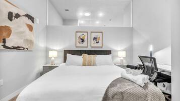 A modern hotel room with a large bed, two bedside lamps, a desk with a chair, and artwork on the walls.