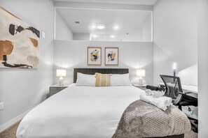 Une chambre d’hôtel moderne avec un grand lit, deux lampes de chevet, un bureau avec une chaise et des œuvres d’art accrochées aux murs.