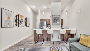 Una cocina moderna con una isla central, taburetes de bar y un área de comedor con sofá gris y alfombra estampada.