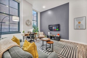 A modern living room with a grey sofa, yellow cushions, a round wooden coffee table, a TV mounted on the wall, and a patterned rug.