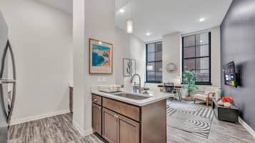 A modern kitchen with a central island, a dining area with a sofa and table, and a large window providing natural light.