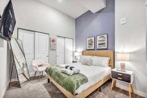 A neatly arranged bedroom with a bed, bedside tables, a chair, and artwork on the walls.