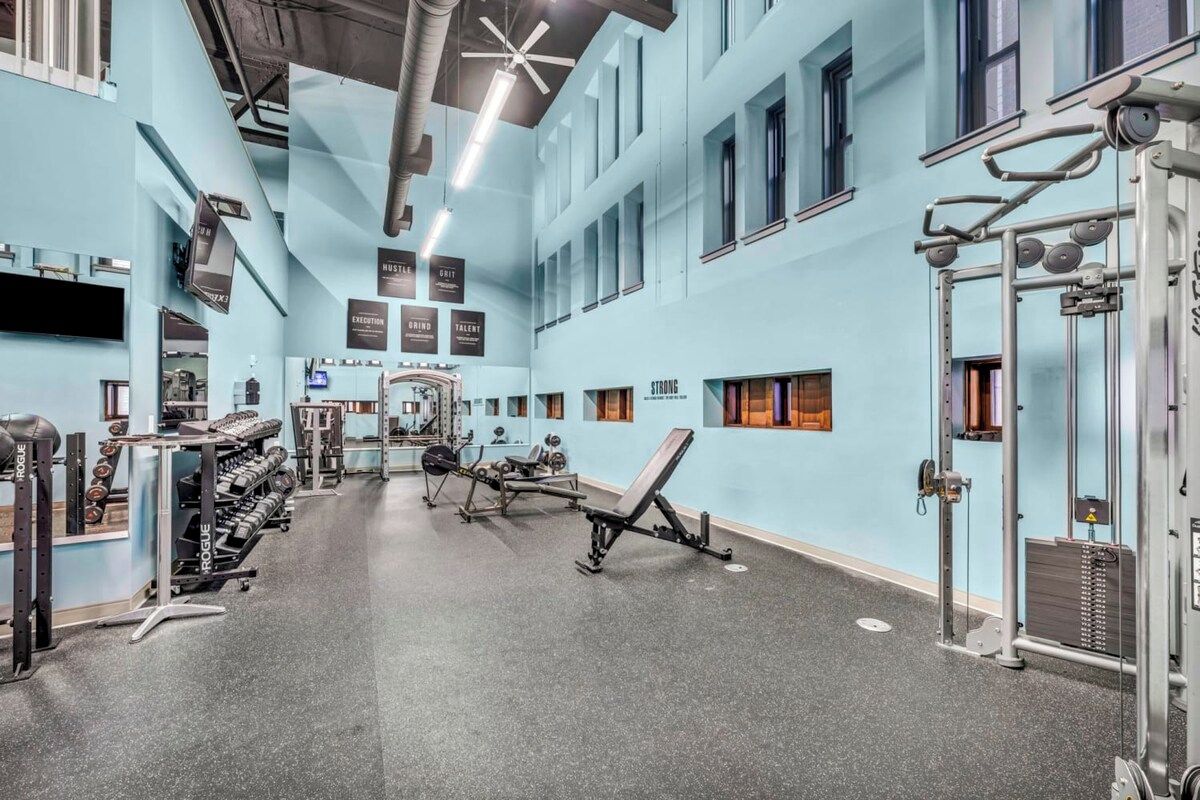 Un gimnasio con equipo de levantamiento de pesas, espejos y carteles motivacionales en las paredes.