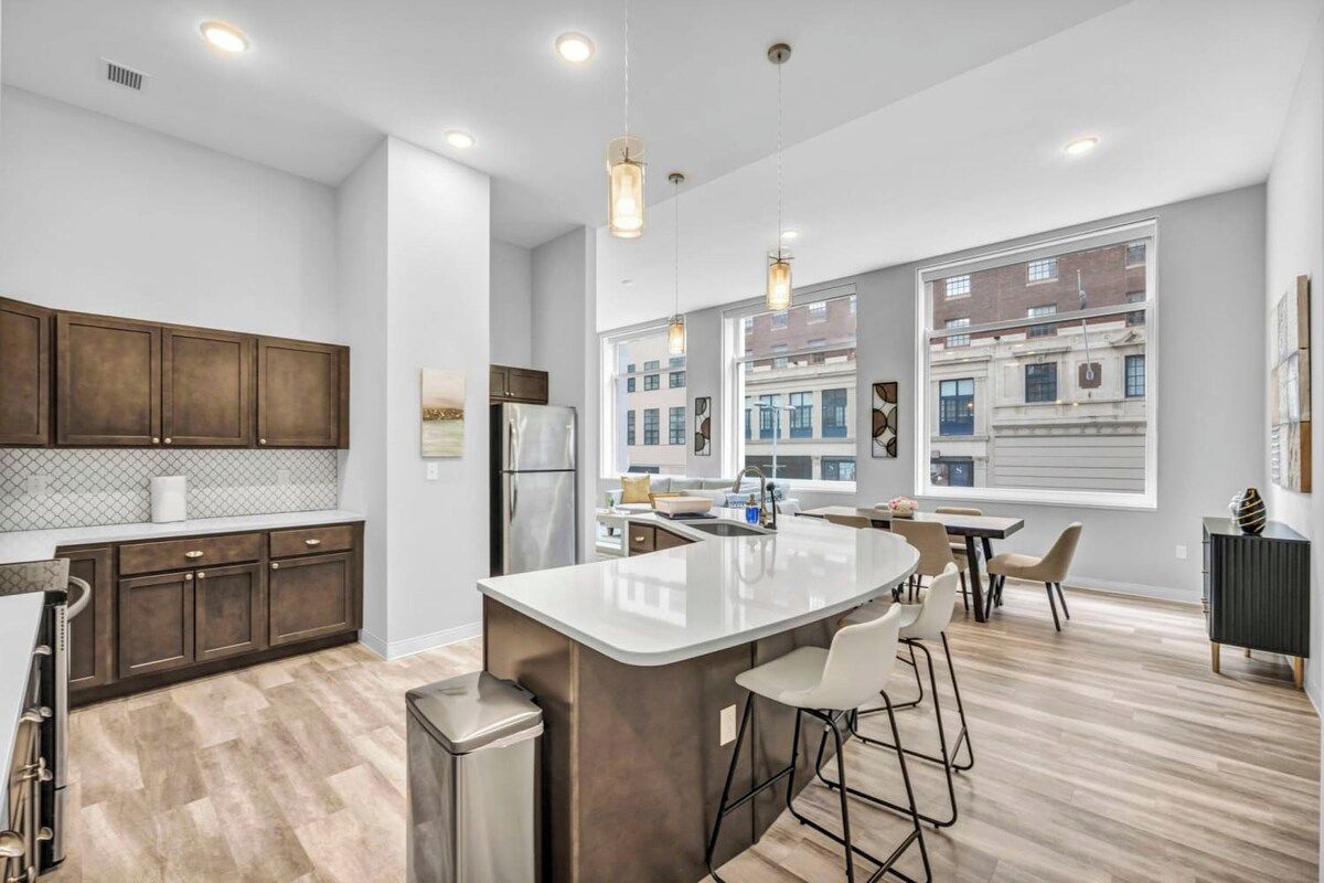 A modern kitchen with a central island, bar stools, and a view of the city through large windows.