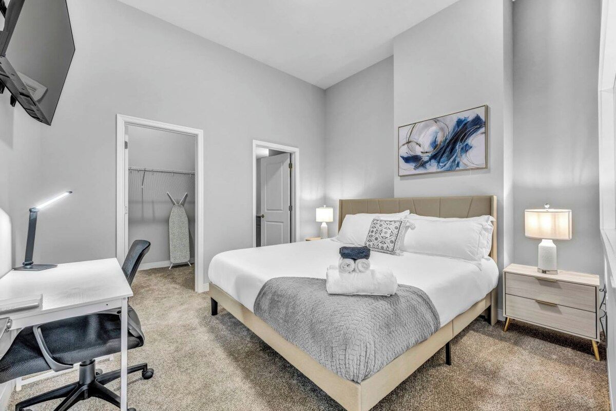 A hotel room with a bed, desk, chair, and a TV.