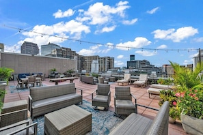 Un patio al aire libre con mobiliario de mimbre, plantas en macetas y vista panorámica de la ciudad.