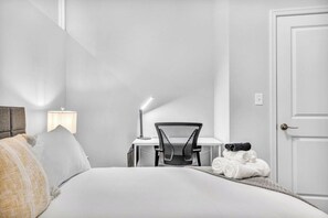 A hotel room with a bed, a desk with a chair, a lamp, and a door. - Central Flat w/ Pool & Sauna • Gym•Heart of DT (Cleveland)