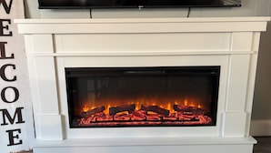 Una chimenea blanca con frente de vidrio, un televisor de pantalla plana montado encima y un letrero que dice 'WELCOME' a la izquierda.