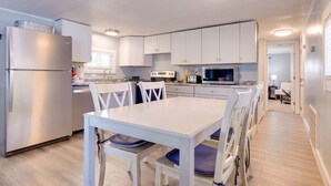 Una cocina compacta con gabinetes blancos, un refrigerador de acero inoxidable, un microondas y una estufa. Cuenta con una mesa de comedor con sillas y una ventana sobre el lavamanos.