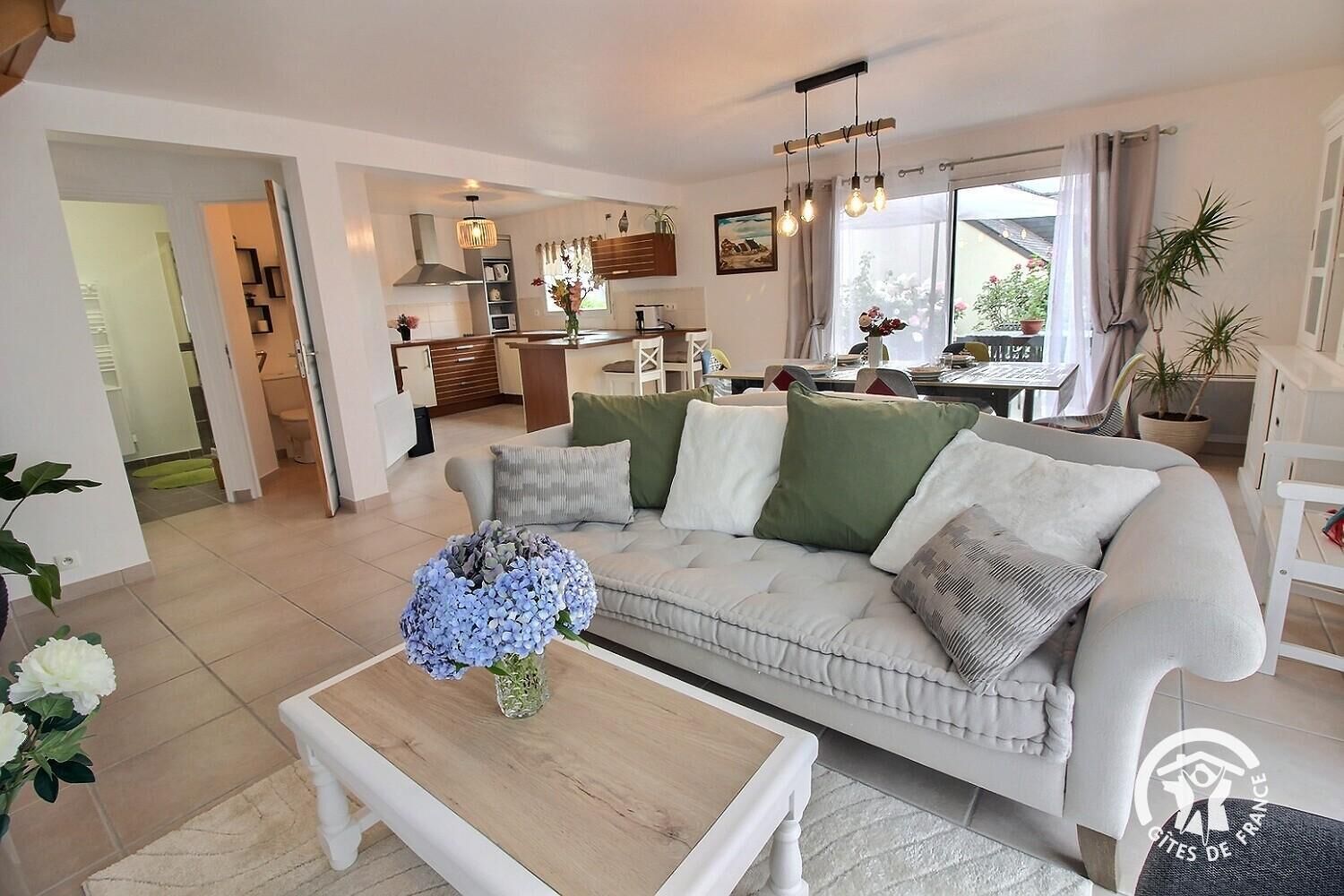 A modern living room with a sofa, coffee table, and a dining area in the background.