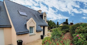 A house with a sloped roof, a small window, and a garden with red flowers.