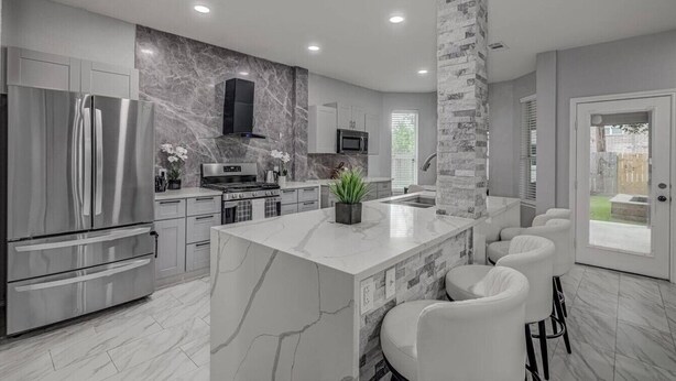 A modern kitchen with a central island, stainless steel appliances, and a stone accent wall. - *NEW* Modern Getaway - Houston (Houston)