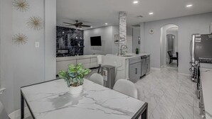 A modern kitchen with a marble countertop, a dining area with a white table, and a built-in island with a sink. - *NEW* Modern Getaway - Houston (Houston)