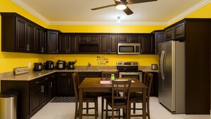 A kitchen with dark wooden cabinets, a stainless steel refrigerator, a microwave, and a stove. There is a dining table with chairs and a small trash can. - Enjoyable apartment with AC in Kingston (Kingston)