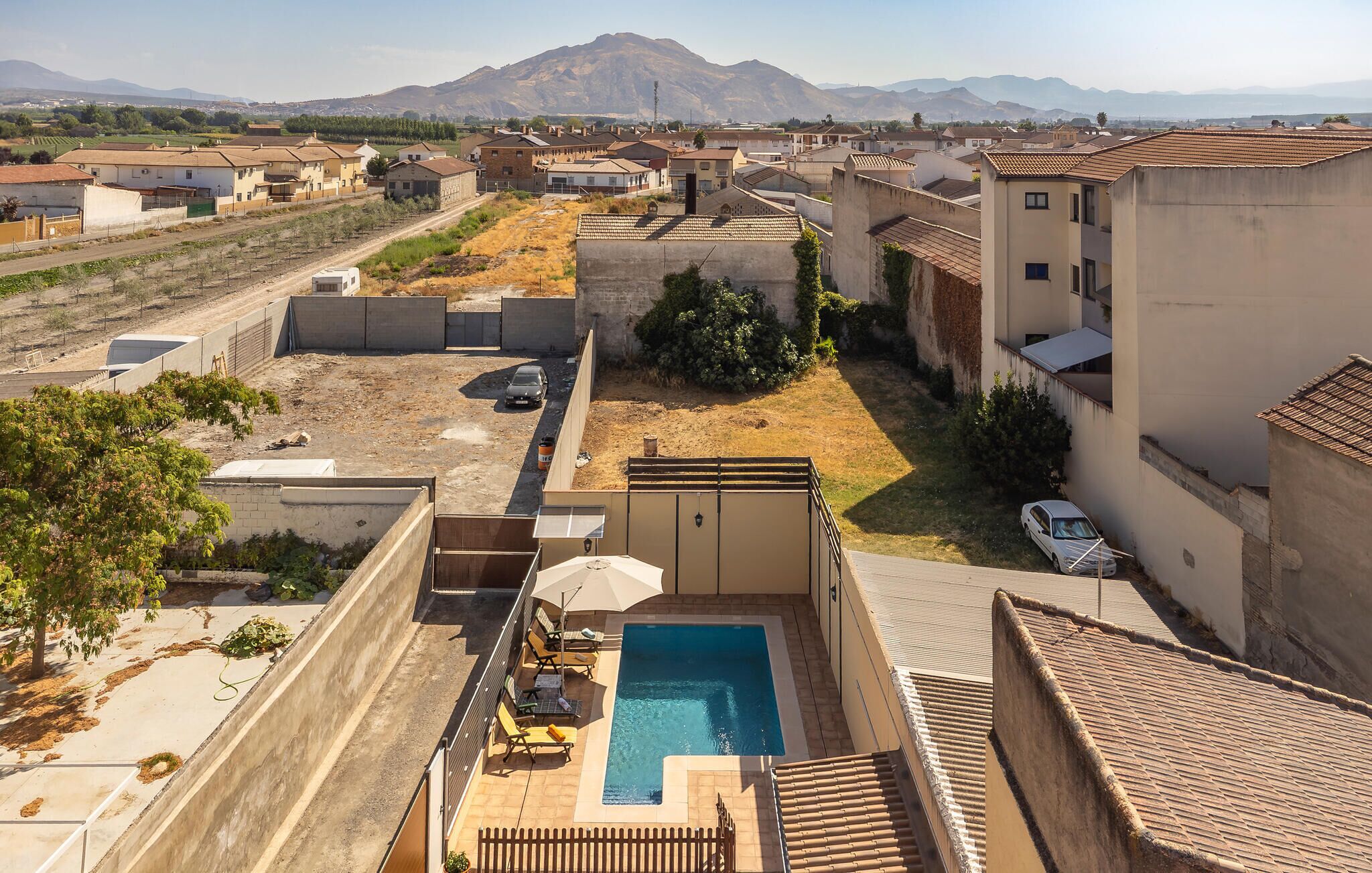 A residential area with a swimming pool, outdoor seating, and a view of distant mountains.