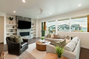 Uma sala de estar moderna com lareira, uma televisão de tela plana e uma grande janela com vista para uma área residencial.