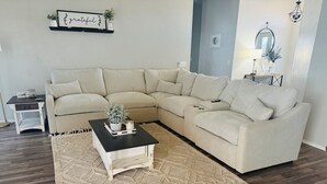 Een woonkamer met een hoekbank, een bijzettafeltje en een vloerkleed.