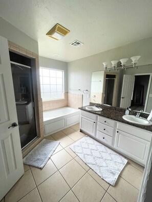 A bathroom with a bathtub, two sinks, a vanity, a window, and a shower. - Your Home Base for Game Days & Getaways!! (Stillwater)
